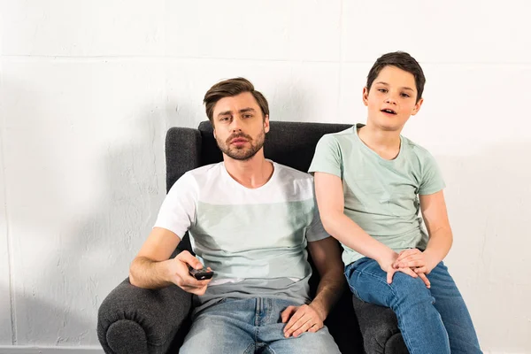 Son and father with remote controller watching tv in living room — Stock Photo