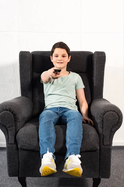 Garçon en jeans assis dans le fauteuil et tenant télécommande — Photo de stock