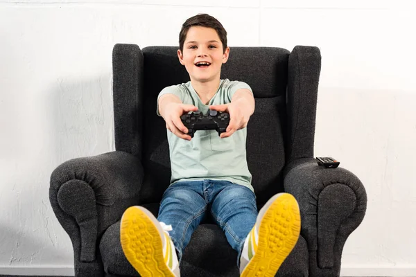 KYIV, UKRAINE - APRIL 17, 2019: excited boy with joystick sitting in armchair and playing video game — Stock Photo