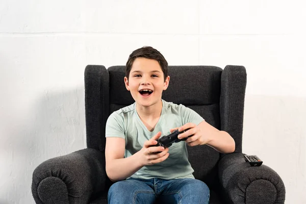 KYIV, UKRAINE - 17 AVRIL 2019 : garçon excité avec joystick assis dans un fauteuil et jouant à un jeu vidéo — Photo de stock