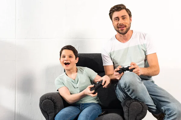 KYIV, UKRAINE - 17 AVRIL 2019 : fils et père souriants tenant des joysticks et jouant ensemble à des jeux vidéo — Photo de stock