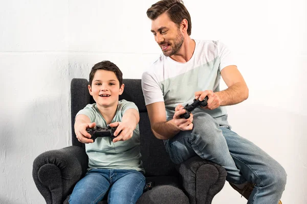 KYIV, UKRAINE - 17 de abril de 2019: filho sorridente e pai segurando joysticks e jogando videogames juntos — Fotografia de Stock