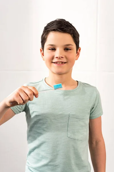 Niño sonriente sosteniendo el cepillo de dientes y mirando a la cámara en el baño - foto de stock