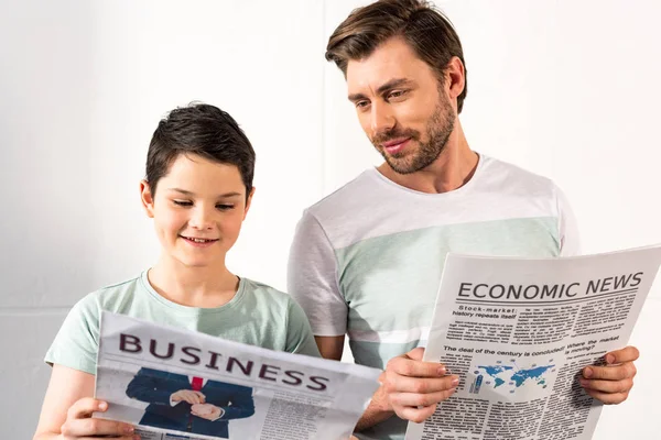 Sonriente hijo y padre leyendo periódicos en casa - foto de stock