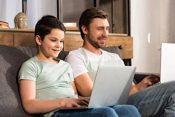 Sorridente figlio e papà utilizzando i computer portatili in soggiorno — Foto stock