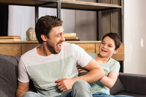 Rire fils et papa assis sur le canapé et s'amuser dans le salon — Photo de stock