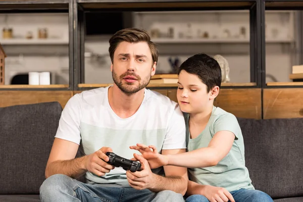 Padre e hijo sentados en el sofá y jugando videojuegos - foto de stock