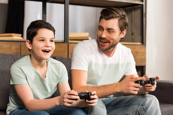 KYIV, UKRAINE - 17 de abril de 2019: pai e filho sorridentes segurando gamepads e jogando videogames na sala de estar — Fotografia de Stock