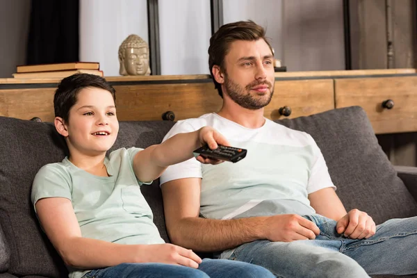 Figlio e padre sorridente con telecomando che guarda la tv in soggiorno — Foto stock