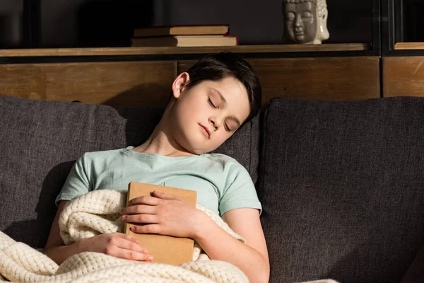 Niño con libro durmiendo bajo manta en sala de estar - foto de stock
