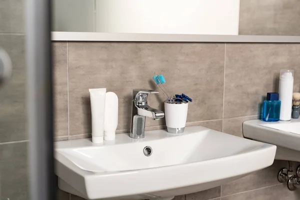 Toothbrushes, toothpaste and shaving razors on sink in bathroom — Stock Photo