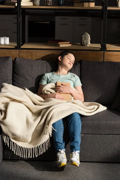 Boy with book sleeping under blanket in living room — Stock Photo