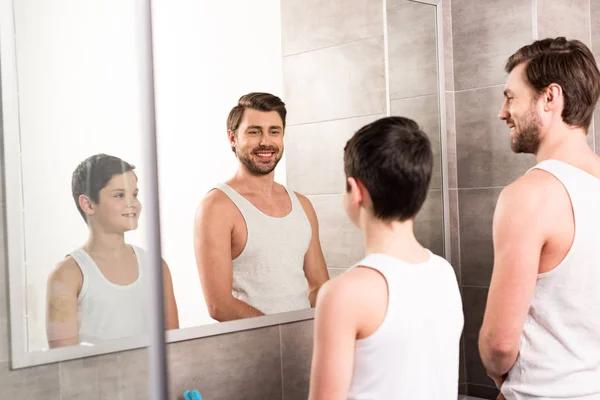Smiling son and dad looking at mirror in bathroom — Stock Photo