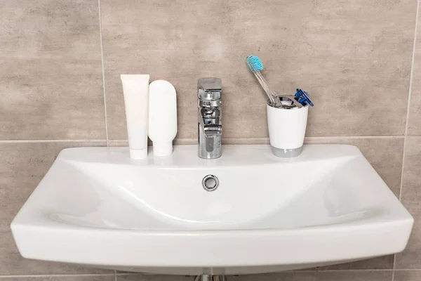 Shaving razors, toothbrush, toothpaste and shampoo on sink in bathroom — Stock Photo