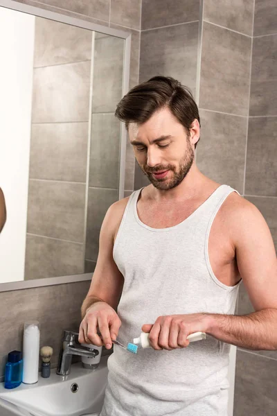 Lächelnder Mann trägt morgens im Badezimmer Zahnpasta auf Zahnbürste auf — Stockfoto