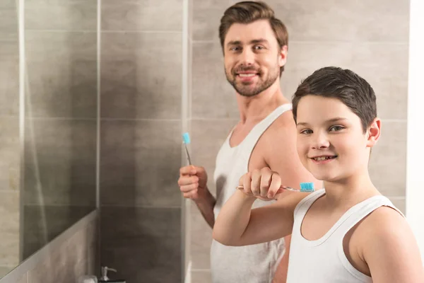 Smiling son and dad brushing teeth in morning in bathroom — Stock Photo