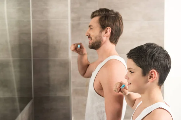 Sorrindo filho e pai escovando os dentes de manhã no banheiro — Fotografia de Stock