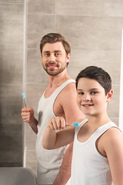 Smiling son and dad brushing teeth in morning in bathroom — Stock Photo