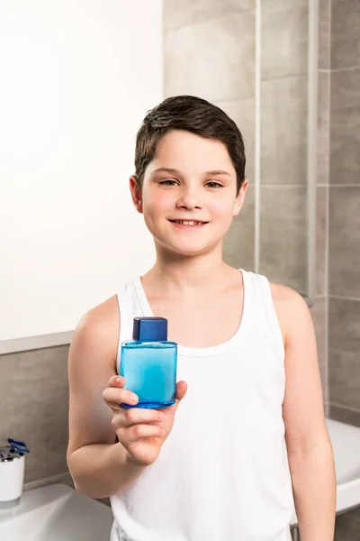 Niño sonriente sosteniendo la loción y mirando a la cámara en el baño - foto de stock