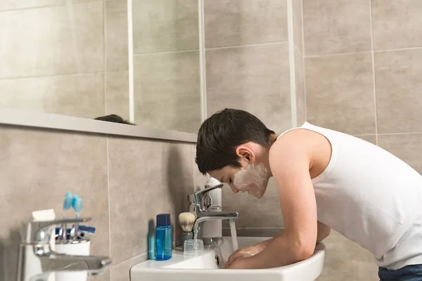 Preteen boy washing face in morning in bathroom — Stock Photo