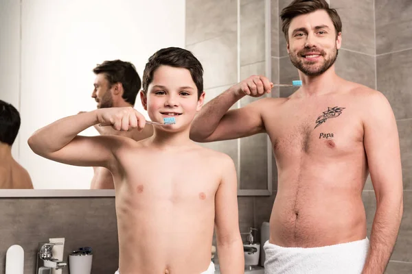 Smiling son and dad brushing teeth in bathroom — Stock Photo