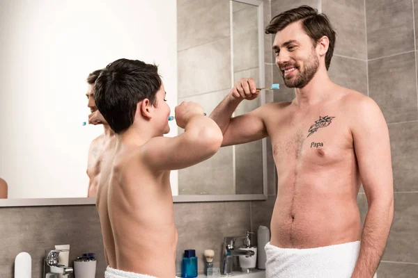 Улыбающиеся сын и папа чистят зубы в ванной комнате — стоковое фото