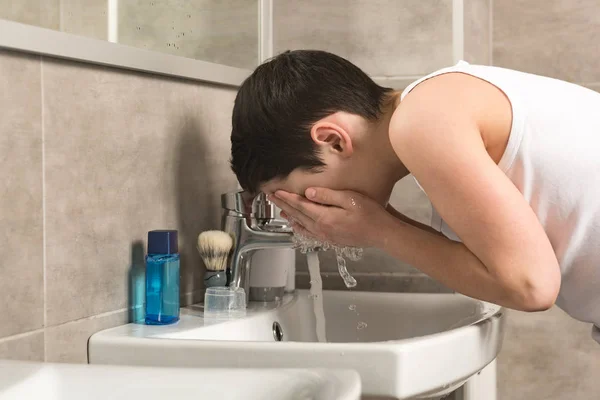 Preadolescente chico lavado cara en la mañana en baño - foto de stock
