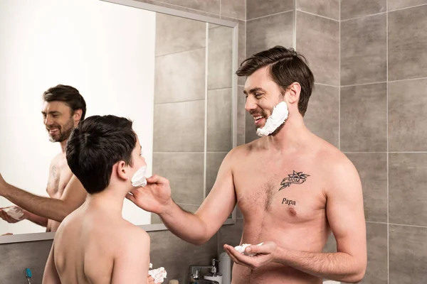 Laughing son and dad applying shaving foam in bathroom — Stock Photo