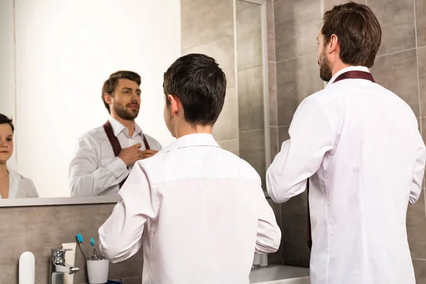 Pai e filho vestir-se em desgaste formal na frente do espelho no banheiro — Fotografia de Stock