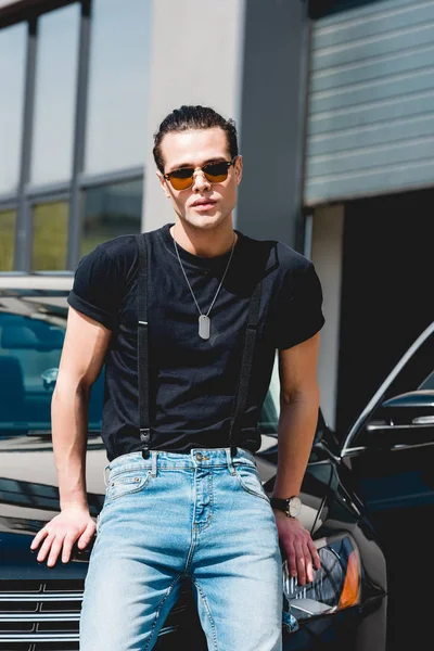 Bello uomo elegante in occhiali da sole e tag cane posa vicino auto — Foto stock