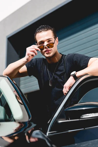 Schöner stylischer Mann mit Sonnenbrille posiert in der Nähe von Auto und schaut in die Kamera — Stockfoto