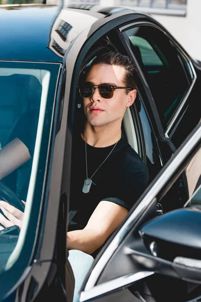 Handsome stylish man in sunglasses with tag dog sitting in car — Stock Photo