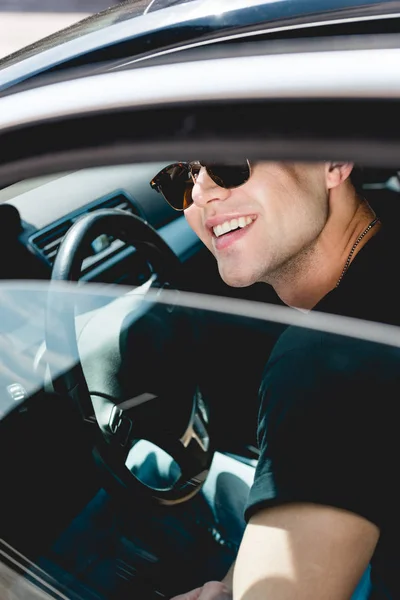 Selektiver Fokus eines gut aussehenden, stylischen Mannes mit Sonnenbrille, der lächelt und im Auto sitzt — Stockfoto