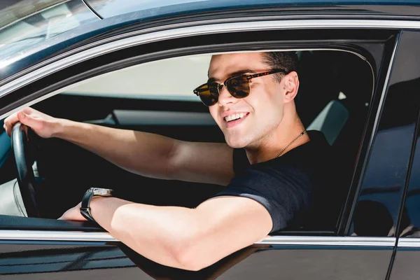 Bell'uomo elegante in occhiali da sole sorridente e seduto in auto — Foto stock