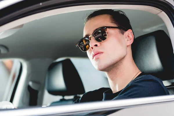 Selektiver Fokus eines gut aussehenden, stylischen Mannes mit Sonnenbrille, der im Auto posiert — Stockfoto