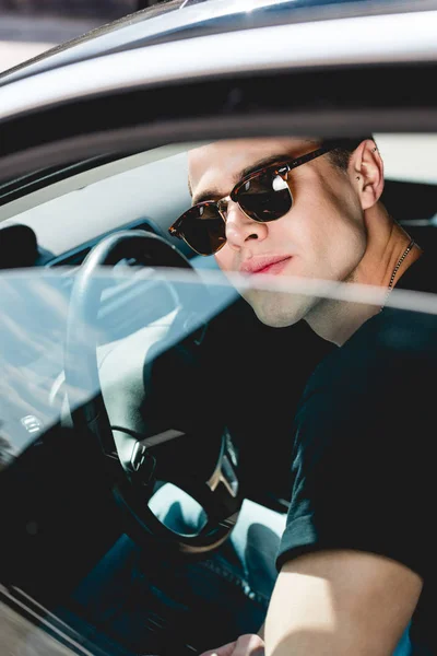 Selektiver Fokus eines gut aussehenden, stylischen Mannes mit Sonnenbrille, der im Auto posiert — Stockfoto