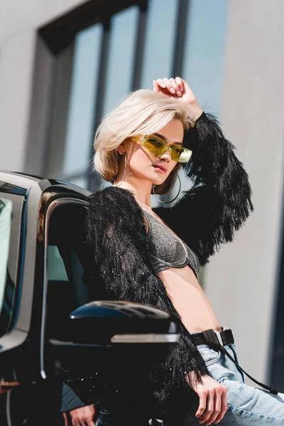 Красива стильна молода жінка в окулярах позує біля машини — стокове фото