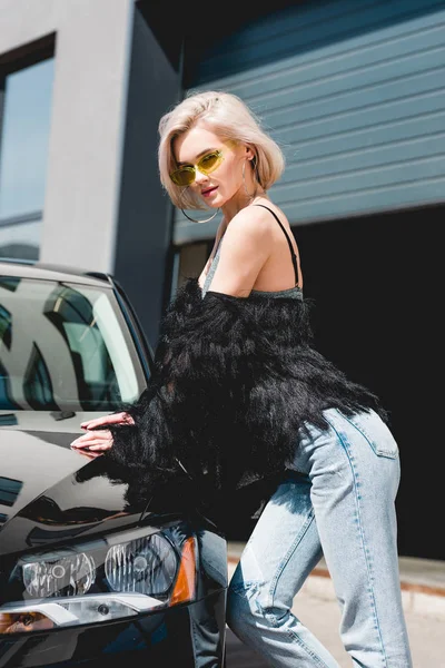 Atractiva mujer joven sexy de moda en gafas posando cerca del coche - foto de stock