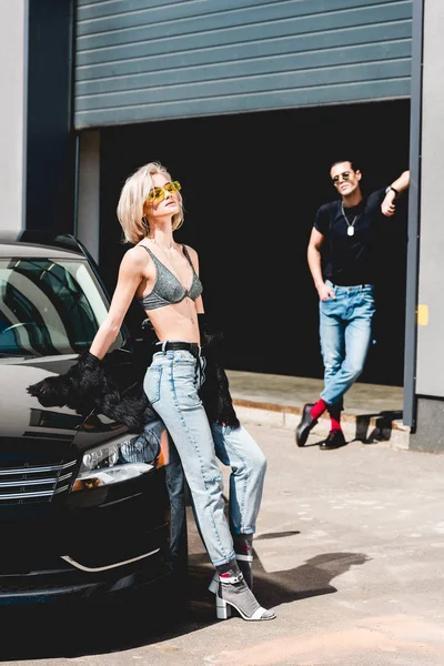 Стильный мужчина и красивая девушка позируют возле машины и гаража — стоковое фото