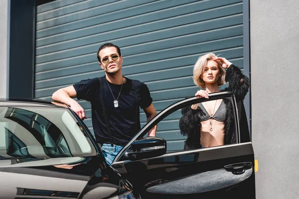 Stylish handsome man and beautiful girl posing near car — Stock Photo