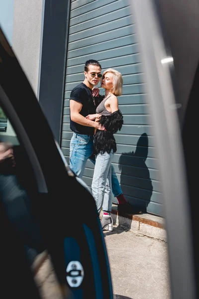 Foco seletivo de homem bonito elegante abraçando menina bonita perto do carro — Fotografia de Stock