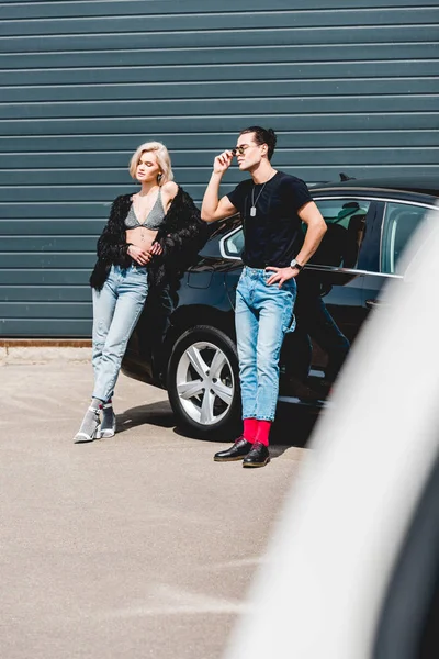 Homme beau à la mode et belle fille posant près de la voiture — Photo de stock
