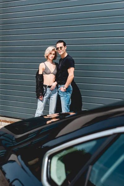 Fashionable handsome man and beautiful girl posing near car — Stock Photo