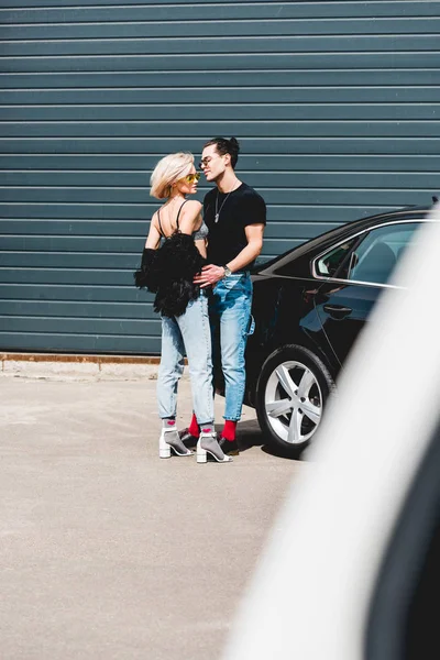 Hombre guapo de moda y hermosa chica posando cerca del coche - foto de stock