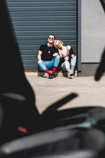 Stylish man and sexy young woman smiling and sitting near garage door — Stock Photo