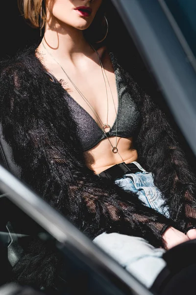 Vista recortada de sexy mujer joven de moda posando en el coche - foto de stock