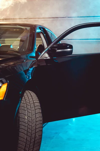 Noir brillant voiture de luxe avec porte ouverte dans le garage avec fumée — Photo de stock