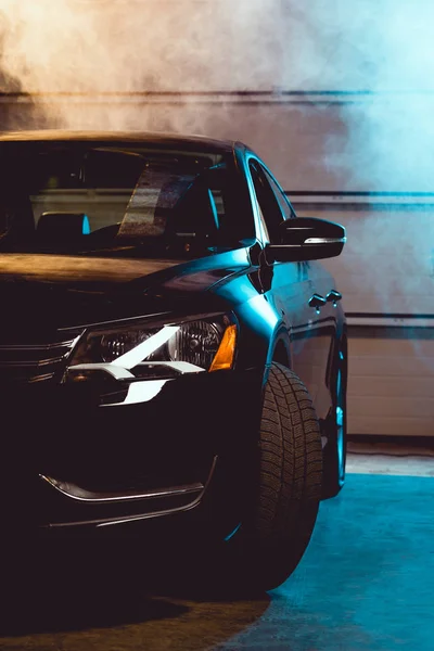 Black shiny luxury car in garage with smoke — Stock Photo