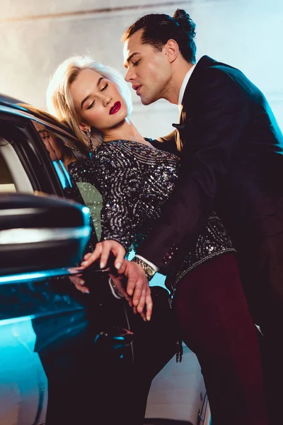 Bel homme élégant et jeune femme sensuelle posant près de la voiture — Photo de stock