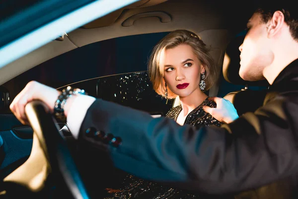 Uomo elegante e bella giovane donna sensuale in abbigliamento formale seduto in auto — Foto stock